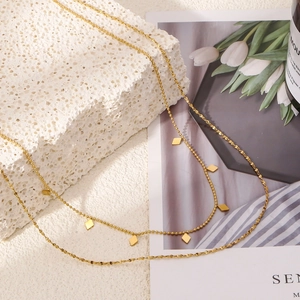 Collier double épaisseur en or avec pendentifs géométriques sur fond de pierre blanche chic