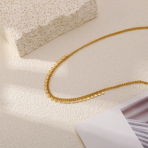 Detalle de un collar de cadena dorada minimalista con pequeñas lentejuelas en una piedra