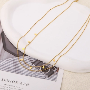 Détail d'un collier doré double épaisseur avec pendentifs losanges sur plateau blanc