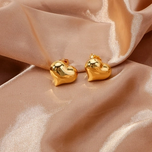 Polished 3D gold heart stud earrings displayed on elegant champagne satin silk fabric