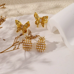 Elegant gold butterfly and pearl pineapple stud earrings set on a white surface