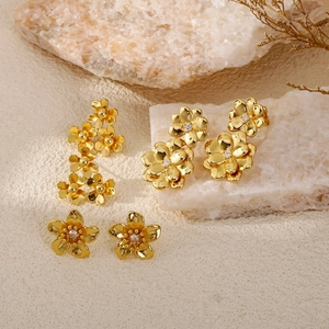 Elegant gold flower stud earrings with white gemstones displayed on stone and sand base