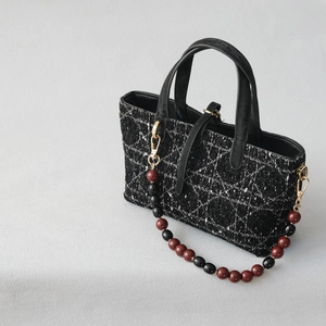 Detail of tweed tote bag with quilted pattern and decorative red and black beaded strap