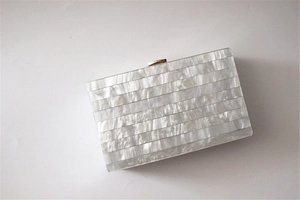 Detail of white striped pearlescent acrylic evening clutch with gold metal buckle