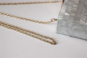 Close-up detail of acrylic evening bag with striped pearlescent texture and gold chain link