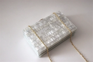Close-up of pearl acrylic evening bag with gold chain strap and striped texture