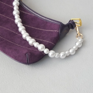 Détail du sac en daim violet avec coutures ondulées et poignée en perles dégradées