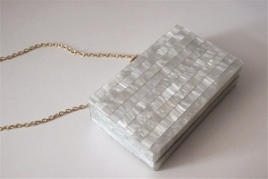 Detail view of pearlescent acrylic evening clutch with gold chain and marble texture