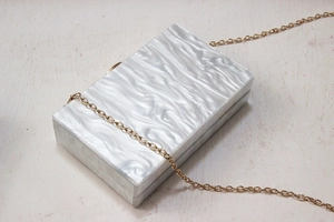 Detail of pearlescent marble acrylic clutch bag with elegant golden chain strap