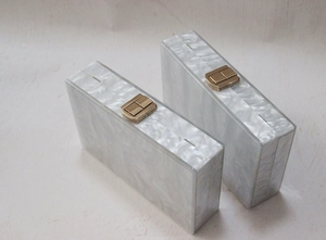 Detail showing the golden metal clasp and pearlescent acrylic texture on box clutch bag