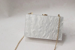 Detail of white marble texture acrylic clutch bag with elegant golden chain and clasp