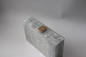 Detail of gray marble acrylic clutch bag featuring polished gold metal rectangle clasp