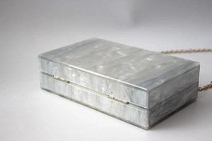 Detail of grey marble acrylic clutch bag showing gold metal hinge and fine chain strap