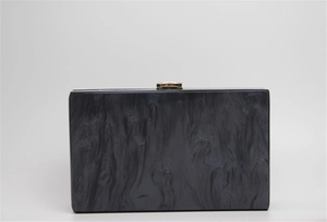Macro detail of black marble textured acrylic clutch bag with a golden metal snap closure