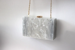 Detail of grey marble pattern acrylic clutch bag with elegant gold chain and metal clasp
