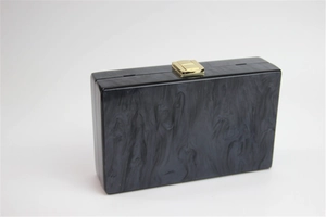 Macro detail of acrylic evening clutch with black marble texture and gold metal clasp