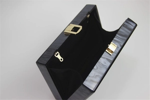 Detail of marble acrylic clutch bag with golden metal clasp and black lining