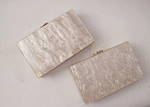Top view of two pearlescent acrylic clutch bags with marble texture and metal clasps