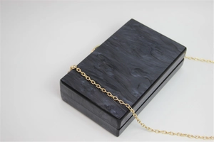 Detail view of acrylic clutch bag featuring black marble texture and gold chain strap