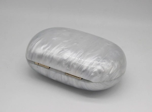 Detailed close-up of oval acrylic evening bag with white marble texture and gold hinges