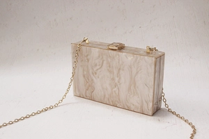 Detail of cream marble acrylic clutch bag with golden metal clasp and chain strap