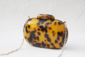 Close-up of tortoise shell acrylic clutch bag with glossy finish and gold chain strap