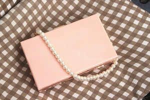 Pink rectangular hard shell clutch bag with gold metal frame and large pearl handle strap