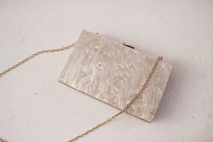 Detail of pearlescent acrylic evening clutch with marble texture and gold chain strap