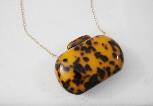 Detail of round leopard print acrylic clutch with glossy tortoiseshell texture and gold chain