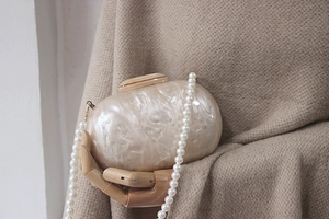 Detail of elegant acrylic clutch with pearl strap held by a wooden hand model