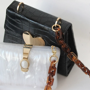 Detail of amber acrylic chunky chain strap on black crocodile and white marble textured bags