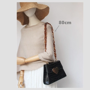 Detail of a black croc-pattern shoulder bag with heart buckle and 80cm amber resin chain