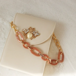 Detail of elegant cream handbag with golden bee clasp and pink resin chain link strap
