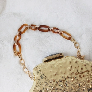 Detail of golden hammered texture evening clutch bag with resin link handle