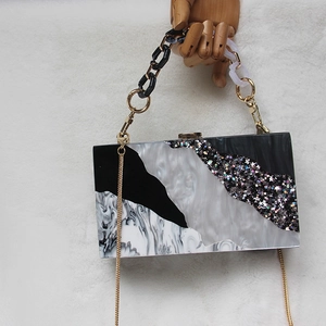 Detail of acrylic evening clutch with marble patterns and shimmering sequins on white velvet