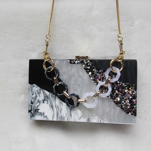 Detail of acrylic clutch with marble texture, star sequins, and resin chain strap