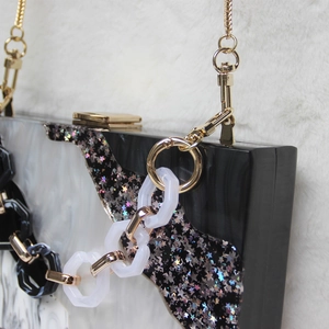Detail of acrylic clutch bag with star glitter pattern and dual chain strap design