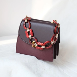 Detail of burgundy leather bag with marble acrylic and gold chain on plush background