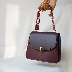 Detail of burgundy lychee leather bag with marble acrylic chain and gold buckle