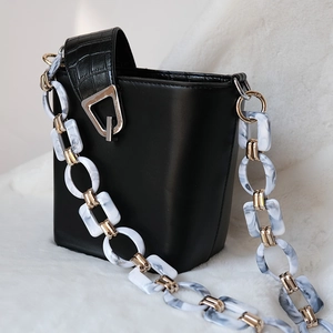 Detail of black bucket bag featuring marble acrylic chain links and crocodile texture strap