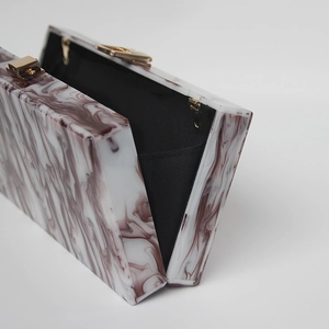 Detail view of marble pattern acrylic evening clutch with gold clasp and black lining