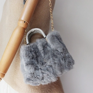 Detail der hellgrauen Webpelz-Handtasche mit goldener Kette und Ledergriff im Fokus