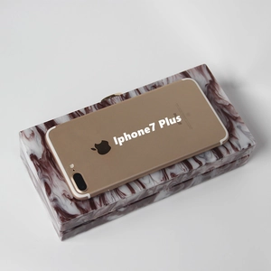 Detail showing the burgundy marble acrylic clutch bag alongside a phone for size reference