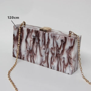 Detail of marble pattern acrylic clutch bag with golden metal chain and press buckle