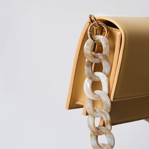 Detailed close-up of acrylic resin chunky chain strap on minimalist smooth beige leather bag
