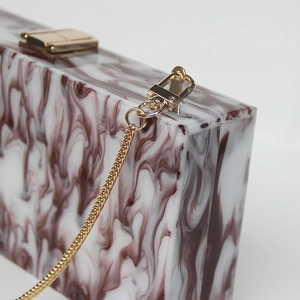Detail of acrylic marble texture clutch bag with golden metal clasp and chain