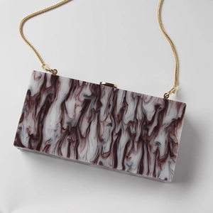 Macro detail of wine red marble texture on acrylic evening clutch bag with gold chain