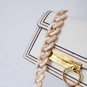 Detail view of cream leather crossbody bag with marbled resin chain and golden hardware