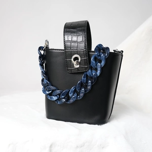 Detail of blue marble acrylic chain and crocodile embossed handle on black leather bag