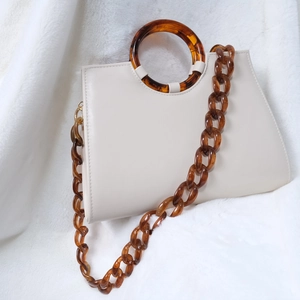 Détail du sac à main en cuir blanc crème avec chaîne en résine ambrée sur fausse fourrure